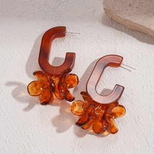 Detail of amber resin flower earrings with C-shaped top on textured stone background
