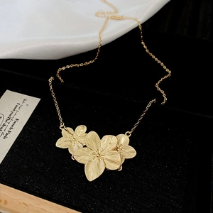 Detailed close-up of matte gold flower necklace featuring refined brushed metal texture
