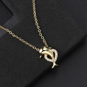 Gold dolphin necklace with heart-shaped zircon pendant on a black textured background