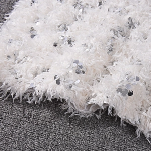Detailaufnahme von weißem Fransenstoff mit silbernen Pailletten und flauschiger Textur