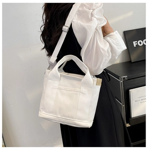 Detail showing the white canvas tote bag with adjustable strap worn by a model in a room