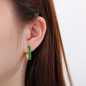 Detail of gold geometric hoop earrings featuring an emerald green rectangular gemstone