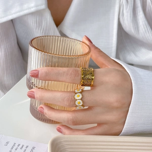 Golden wide portrait ring and daisy enamel ring set shown on hand in a soft morning light