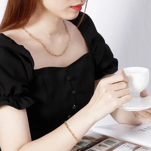 Elegant gold paperclip chain necklace and bracelet set worn by a model in a cafe