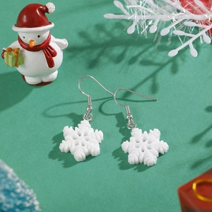 Close-up of white snowflake earrings on a green festive background with Christmas props
