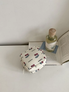 Detail of a square canvas makeup bag with red cherry patterns and a white zipper closure