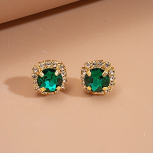 Luxury gold earrings with round green crystal and halo diamonds on beige background