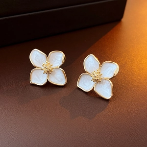 Vue macro de boucles d'oreilles fleur dorées avec émail nacré blanc sur cuir marron