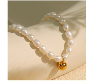 Detail of freshwater pearl necklace with a polished gold ball pendant on beige texture