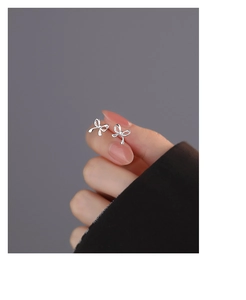 Detailed close-up showing a pair of mini silver bow earrings held on a fingertip for size