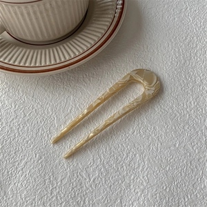 Détail d'une épingle à cheveux en U en acétate marbré crème sur un fond blanc texturé