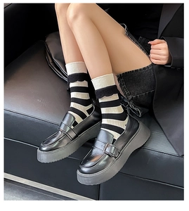 Close-up of black platform loafers and striped knit socks worn by a model on a leather sofa