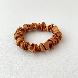 Detailed view of bronze satin scrunchie with pleated texture on white leather