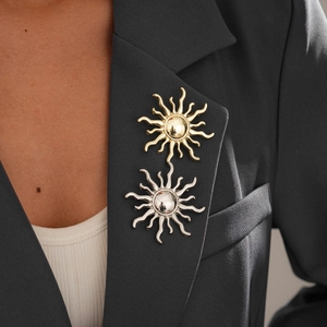 Detail of sun-shaped gold and silver brooches on a black blazer lapel with metallic finish