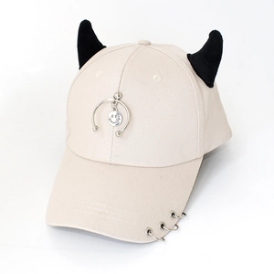 Detail of beige baseball cap featuring black demon horns and metal ring embellishments