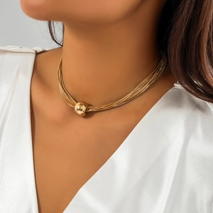 Close-up of gold layered punk chain necklace with a spherical pendant on a model