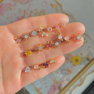 Close-up of golden stud earrings featuring opal stones and heart tassel details