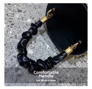 Detail of the black leather bag featuring a unique scrunchie handle and gold metal hardware