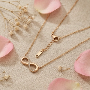 Macro shot of gold infinity pendant with rhinestones on beige fabric with petals