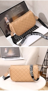 Close-up of beige quilted cylinder bag with wide printed shoulder strap and metal logo
