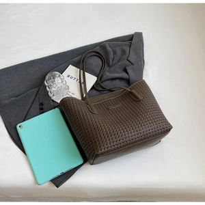 Detailed view of dark brown woven tote bag on bed with modern lifestyle accessories