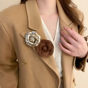 Detail of camellia flower brooches in metallic gold and brown suede on a beige coat lapel