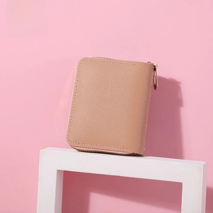 Detail of a dusty pink compact wallet with pebble leather texture and gold zipper