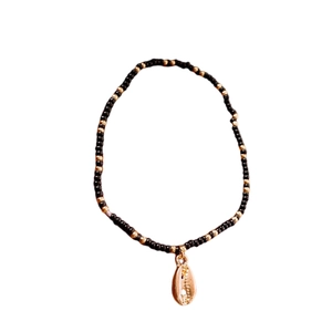 Bohemian black and gold beaded anklet with a shell charm on a plain white background