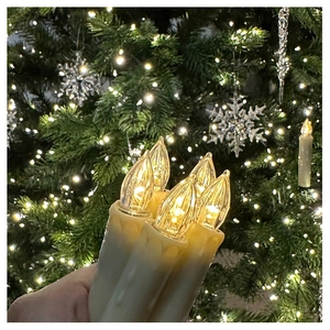 Detail of warm yellow LED candle lamp with realistic dripping wax design on Christmas tree