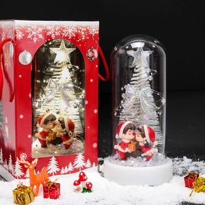 Christmas glass dome with LED white tree and kissing couple next to festive red gift bag