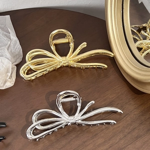 Close-up of elegant gold and silver metal bow hair claws on a vintage wooden surface