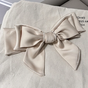 Elegant beige satin bow hair clip with delicate pearls on a soft textured background