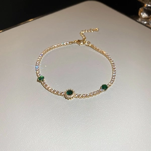 Vue macro détaillée d'un bracelet en or avec des diamants étincelants et des pierres vertes