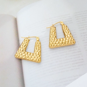 Macro detail of 18K gold plated U-shaped earrings with hammered texture on a book