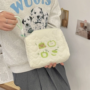 Detail of cream quilted makeup bag with green apple embroidery and mint green wrist strap