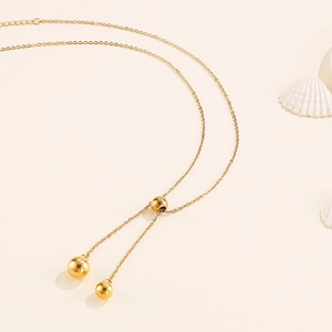 Minimalist Y-shaped stainless steel bead necklace with gold ball pendants on beige background