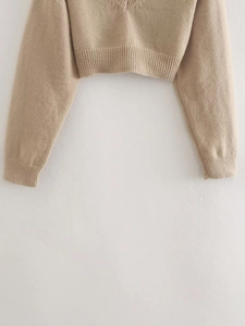 Detailed view of beige cropped knit sweater showing ribbed cuffs and soft fabric texture