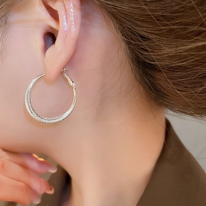 Détail macro de créoles argentées mates avec texture givrée sur le mannequin femme