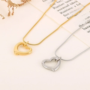 Flat lay of gold and silver hollow heart necklaces with snake chains on beige fabric