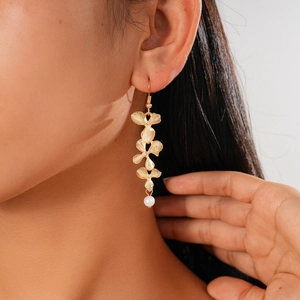 Detail of flower petal gold earrings with pearl drop on model showing the metallic texture