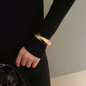 Close-up of a minimalist chunky gold round bracelet with high-polish finish on a black sleeve