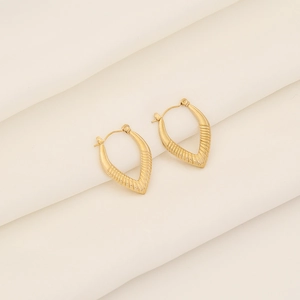 Close-up of golden geometric V-shaped earrings with horizontal texture on white silk fabric