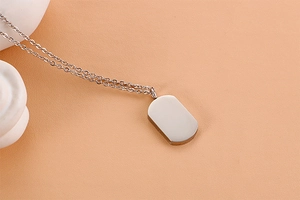 Detail view of a silver stainless steel dog tag pendant with a fine link chain on peach surface