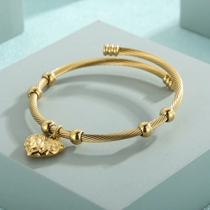 Detail of a gold twisted cable bangle featuring small beads and a heart pendant charm