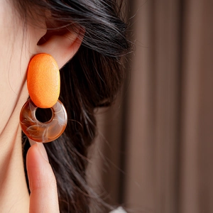 Detail of geometric resin earrings with orange oval top and brown tortoiseshell ring hoop