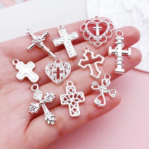 Detail of assorted silver alloy cross pendants with various patterns held in palm
