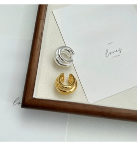 Detailed view of gold and silver triple-layered C-shaped ear cuffs on aesthetic prop background