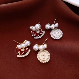 Detailed close-up of pearl earrings with rocking horse and cross pendants on red velvet