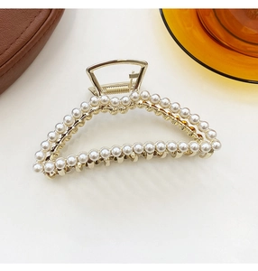 Detail of a gold-tone triangle hair claw clip with faux pearl embellishments on a white desk