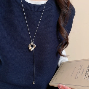 Silberne Halskette mit unregelmäßigem Anhänger auf dunkelblauem Pullover und Buch